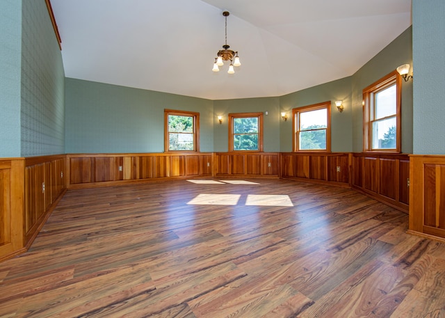 unfurnished room with lofted ceiling, wainscoting, wood finished floors, and a notable chandelier