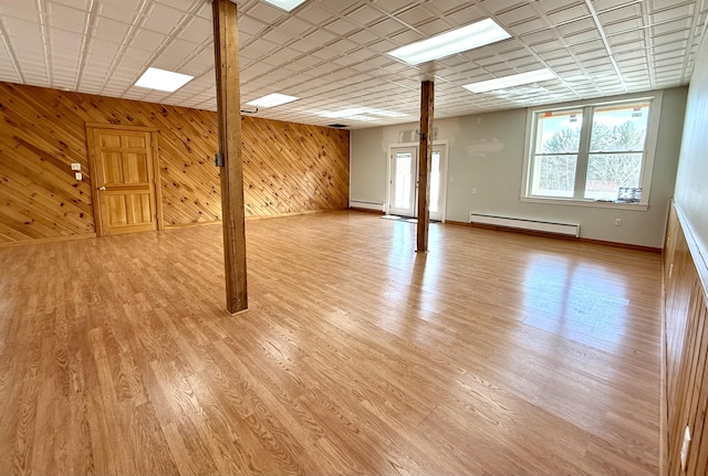 below grade area with baseboards, wood walls, light wood finished floors, and baseboard heating