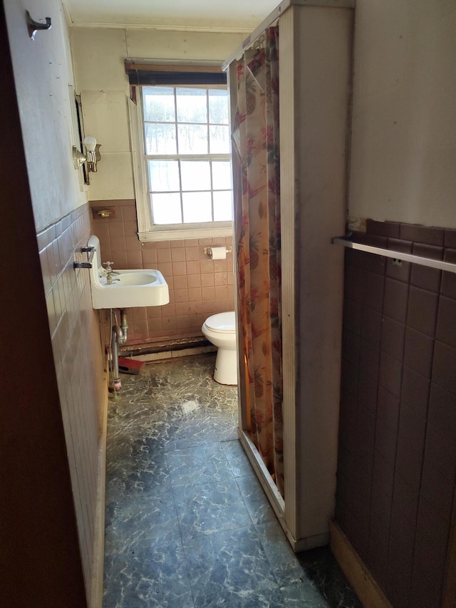 bathroom with a wainscoted wall, a sink, toilet, and tile walls