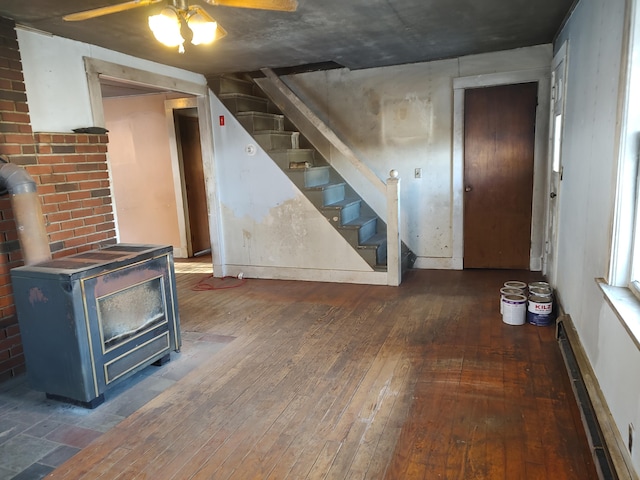 below grade area featuring stairway, a ceiling fan, a wood stove, baseboards, and hardwood / wood-style flooring