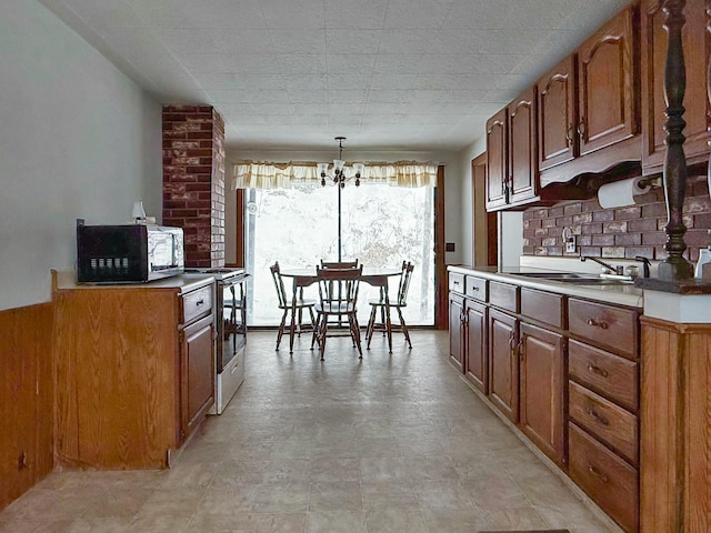 kitchen with brown cabinets, electric range, a sink, and an inviting chandelier