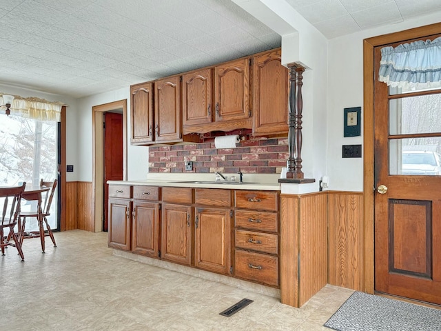 kitchen with visible vents, brown cabinetry, a wainscoted wall, light countertops, and a sink