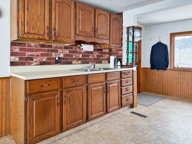 kitchen featuring brown cabinets, a wainscoted wall, visible vents, a sink, and wooden walls