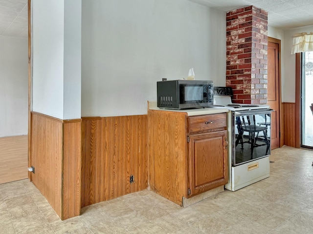 kitchen featuring a wainscoted wall, white range with electric cooktop, light countertops, wooden walls, and black microwave