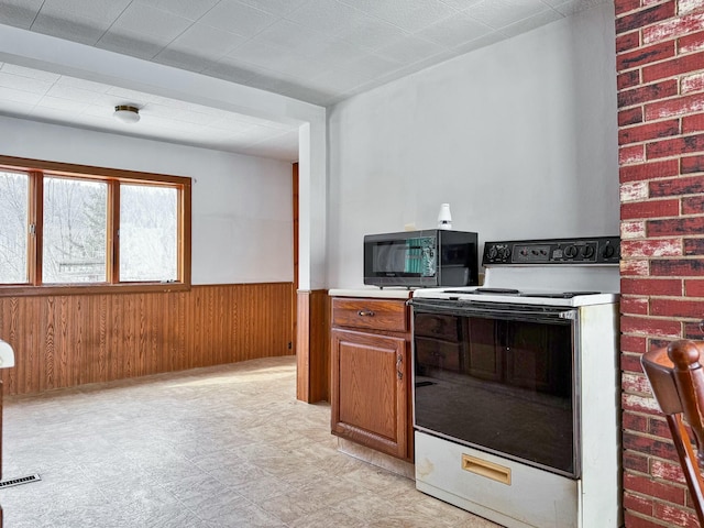 kitchen featuring black microwave, wooden walls, visible vents, electric stove, and wainscoting