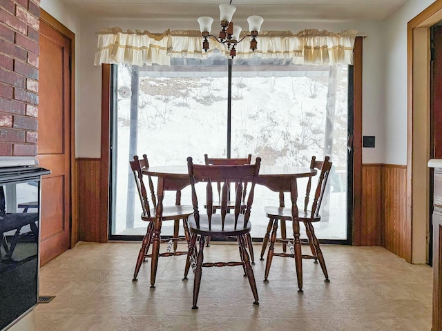 dining space with wood walls, a wainscoted wall, plenty of natural light, and a notable chandelier