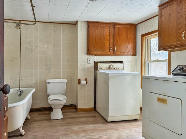 full bath with a freestanding bath, washer / clothes dryer, toilet, and tile walls