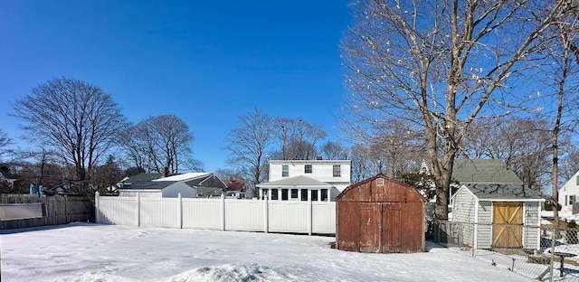 yard layered in snow with a shed, a fenced backyard, and an outbuilding