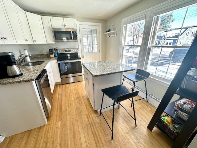 kitchen featuring light wood-style flooring, appliances with stainless steel finishes, white cabinetry, a sink, and light stone countertops