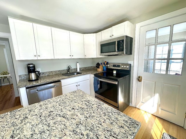 kitchen with appliances with stainless steel finishes, white cabinets, a sink, light stone countertops, and light wood-type flooring