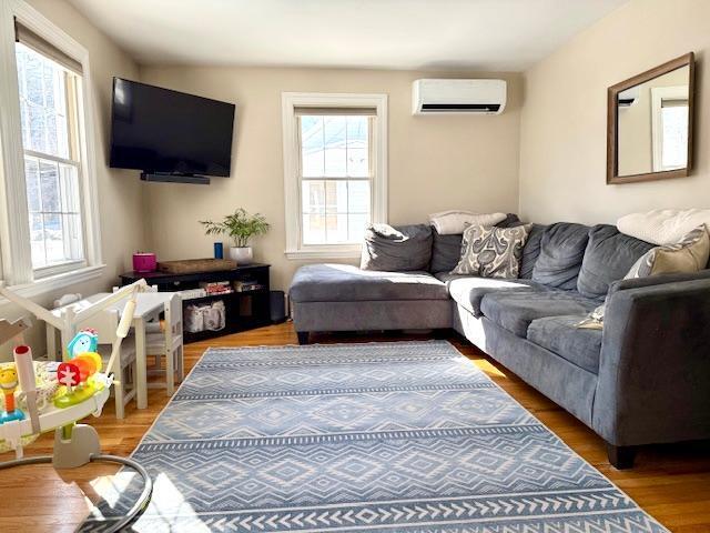 living area with a wall unit AC and wood finished floors