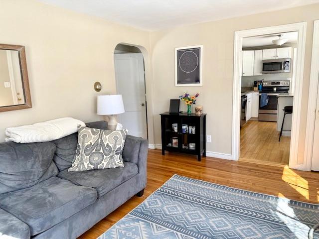 living area with arched walkways, light wood-type flooring, and baseboards