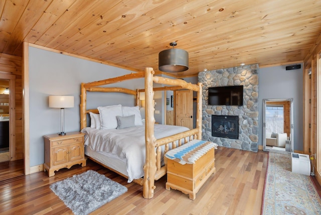 bedroom featuring wooden ceiling, a stone fireplace, and hardwood / wood-style flooring