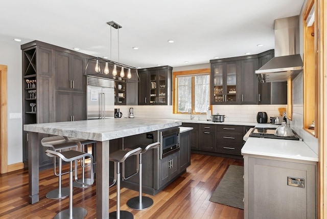 kitchen featuring built in appliances, light countertops, exhaust hood, and a kitchen breakfast bar