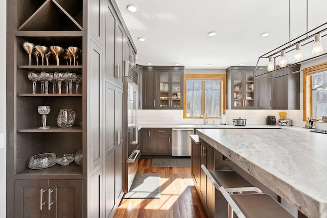 bar featuring a sink, hanging light fixtures, appliances with stainless steel finishes, backsplash, and dark wood-style floors