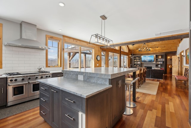 kitchen featuring a center island, open floor plan, wall chimney range hood, wood finished floors, and double oven range