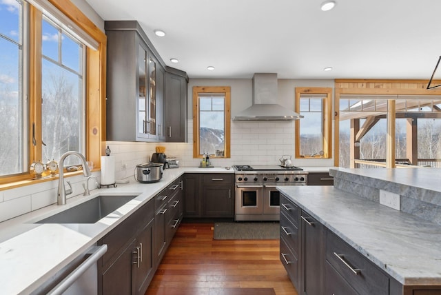 kitchen with dark wood finished floors, wall chimney exhaust hood, white dishwasher, double oven range, and a sink