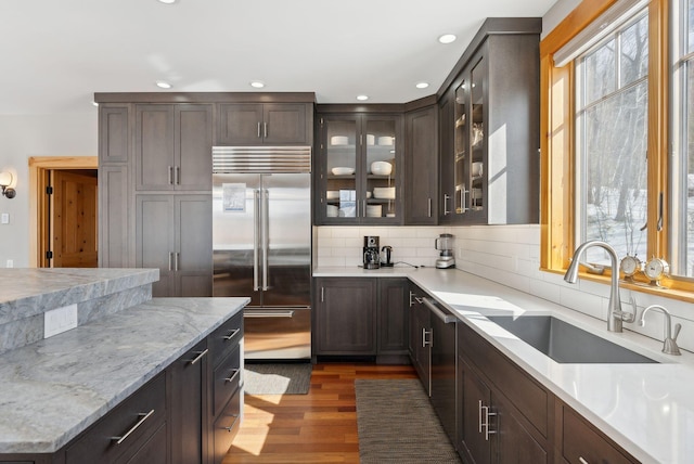 kitchen featuring wood finished floors, a sink, stainless steel built in refrigerator, dark brown cabinets, and backsplash