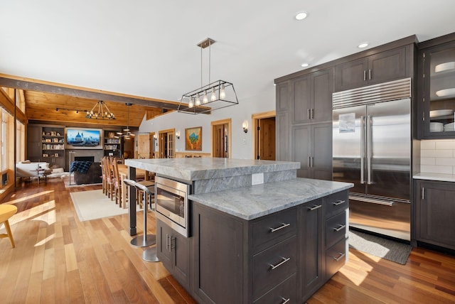 kitchen featuring a center island, a fireplace, light wood-style floors, open floor plan, and built in appliances