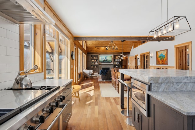 kitchen with cooktop, light wood-style flooring, stainless steel microwave, light stone countertops, and pendant lighting