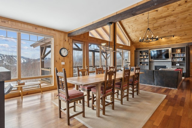 dining area featuring a chandelier, wood-type flooring, a fireplace, and vaulted ceiling with beams