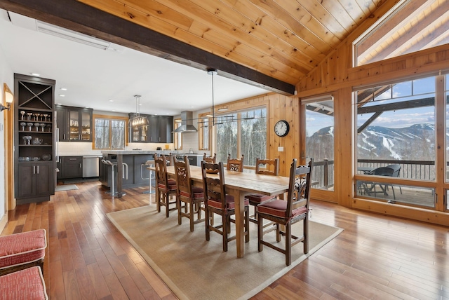 dining space with vaulted ceiling with beams, a mountain view, wood walls, wood ceiling, and hardwood / wood-style floors