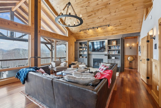 living area with high vaulted ceiling, wooden ceiling, hardwood / wood-style flooring, a notable chandelier, and a glass covered fireplace