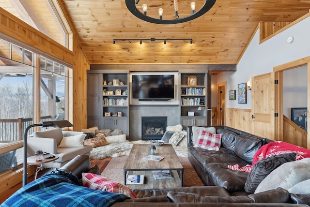 living area with lofted ceiling, wooden walls, wood ceiling, wainscoting, and a glass covered fireplace