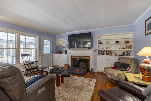 living area with ornamental molding, a glass covered fireplace, dark wood finished floors, and built in features