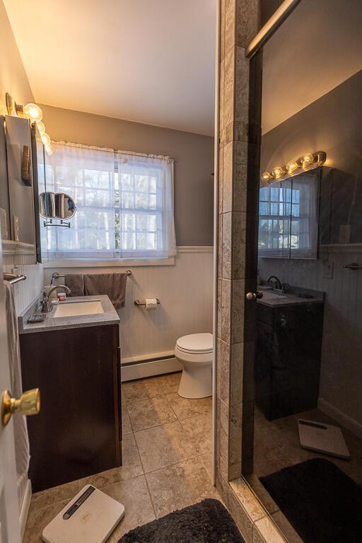 bathroom featuring a baseboard heating unit, a wainscoted wall, vanity, and a stall shower