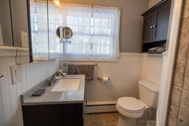 half bath with a baseboard heating unit, a wainscoted wall, vanity, and toilet