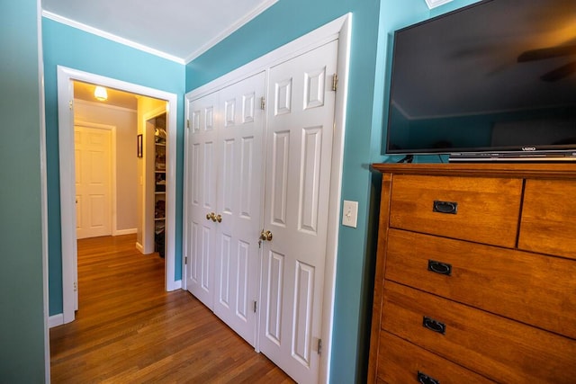 bedroom with a closet, crown molding, baseboards, and wood finished floors