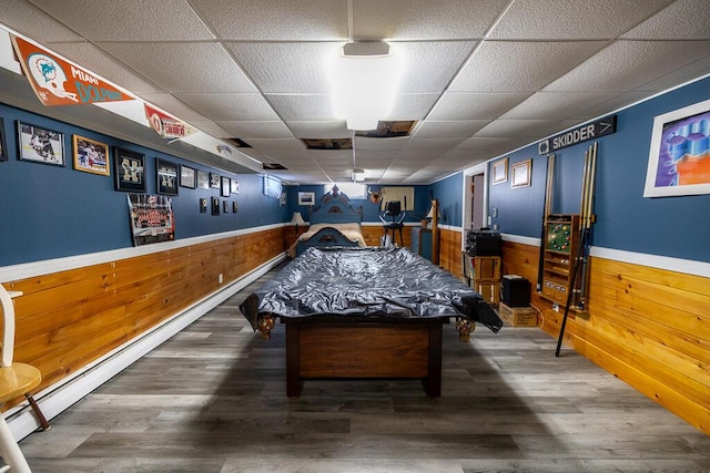 rec room with a wainscoted wall, wood walls, a drop ceiling, and wood finished floors