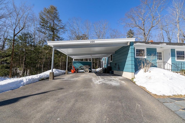 snow covered parking with aphalt driveway and a carport