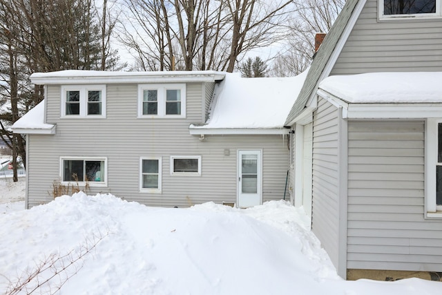 snow covered rear of property featuring a chimney