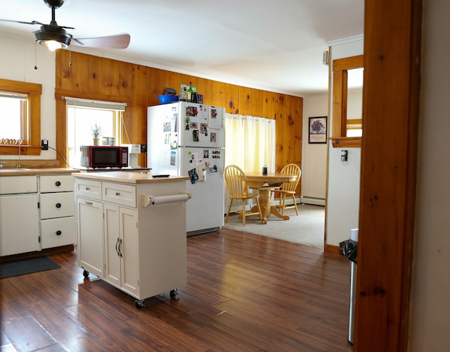 kitchen featuring wooden walls, white cabinets, light countertops, freestanding refrigerator, and dark wood finished floors