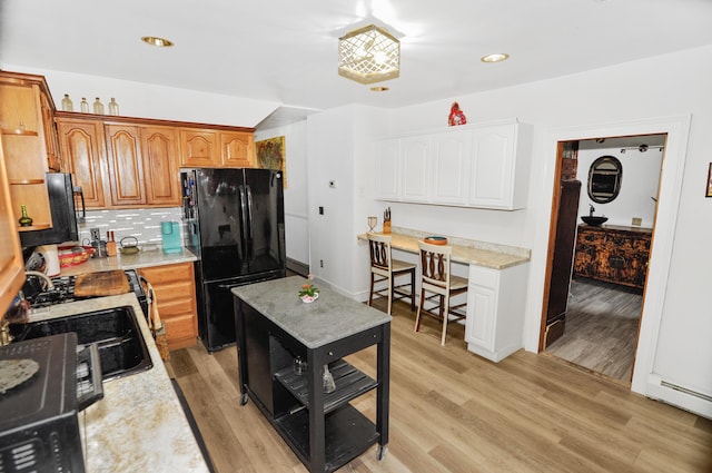 kitchen featuring decorative backsplash, light wood-style flooring, brown cabinets, freestanding refrigerator, and baseboard heating