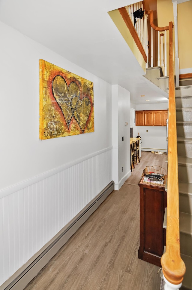 hallway featuring light wood-type flooring, a baseboard radiator, a wainscoted wall, and stairway