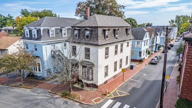 view of front of property featuring mansard roof, a residential view, roof with shingles, and a chimney