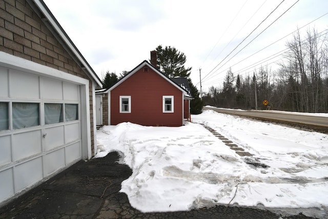 snow covered property with a garage and an outbuilding