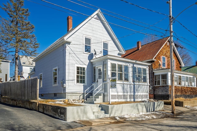 back of house featuring entry steps, fence, a chimney, and a sunroom