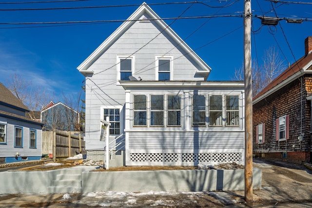 view of front of house with entry steps, fence, and a sunroom