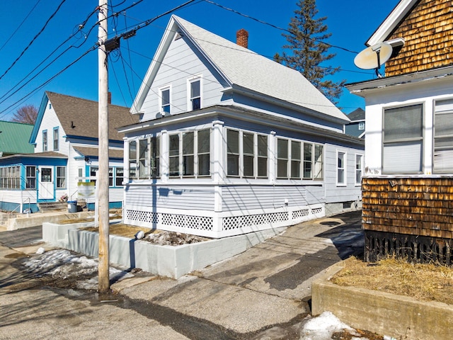 view of front of property with a shingled roof, a chimney, and a sunroom