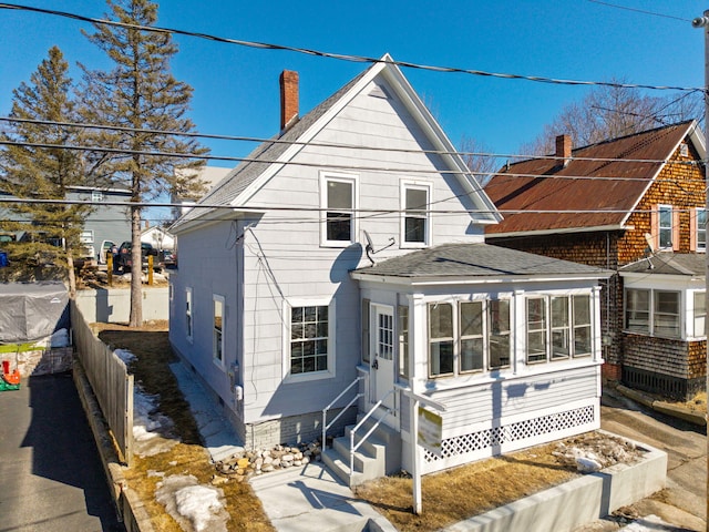 view of front of property with entry steps, fence, roof with shingles, and a chimney