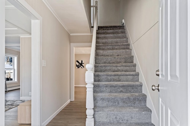 stairs featuring wood finished floors, baseboards, wallpapered walls, a baseboard heating unit, and crown molding