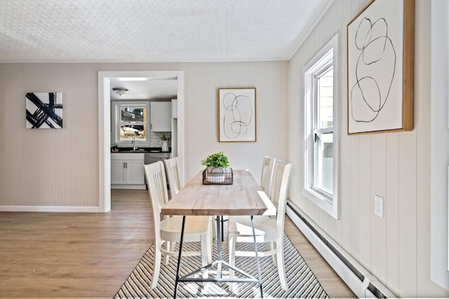 dining room with a textured ceiling, baseboards, baseboard heating, and light wood finished floors