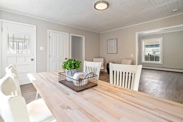 dining area with baseboard heating, wood finished floors, and crown molding