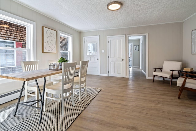 dining area featuring crown molding, wood finished floors, baseboards, and a textured ceiling