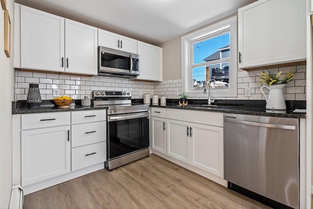 kitchen featuring a sink, appliances with stainless steel finishes, white cabinets, light wood finished floors, and a baseboard radiator