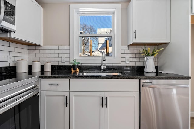 kitchen featuring dark stone counters, a sink, decorative backsplash, stainless steel appliances, and white cabinetry